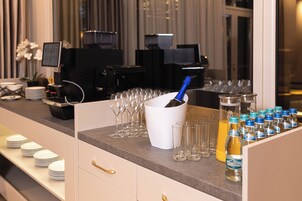 Uma área de bar com máquina de café, uma garrafa de champanhe e uma fileira de copos e garrafas.
