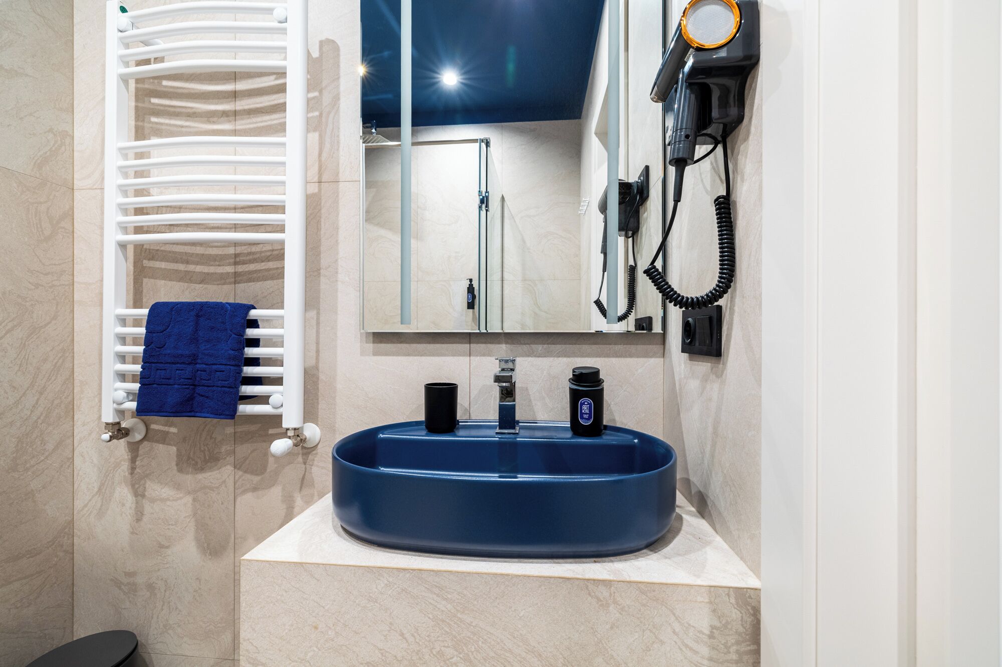 A bathroom with a white towel rack, a blue towel, a blue sink, and a hairdryer mounted on the wall.