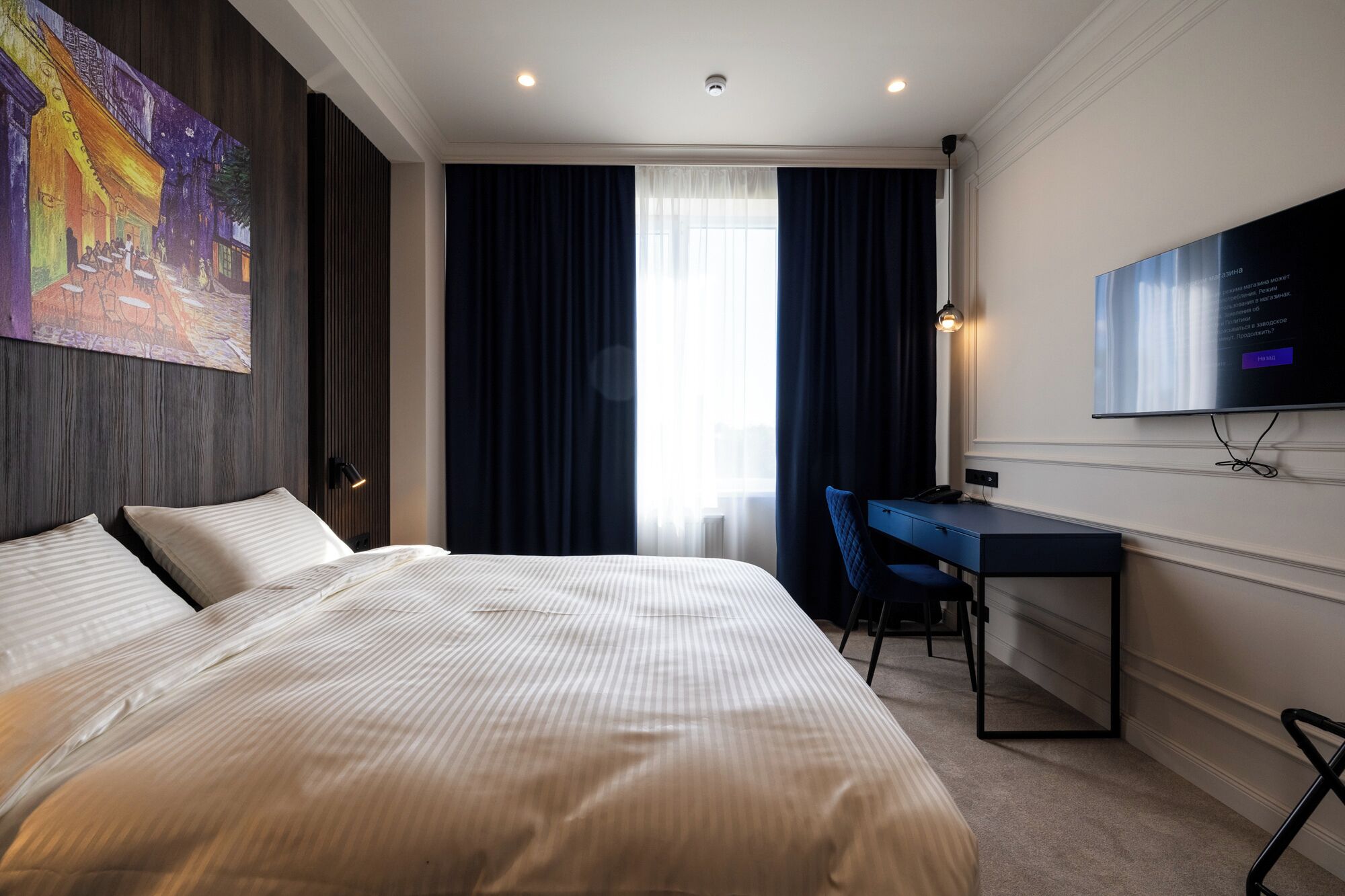 Habitación de hotel con una cama grande, un escritorio, una silla, un televisor montado en la pared y un cuadro en la pared.