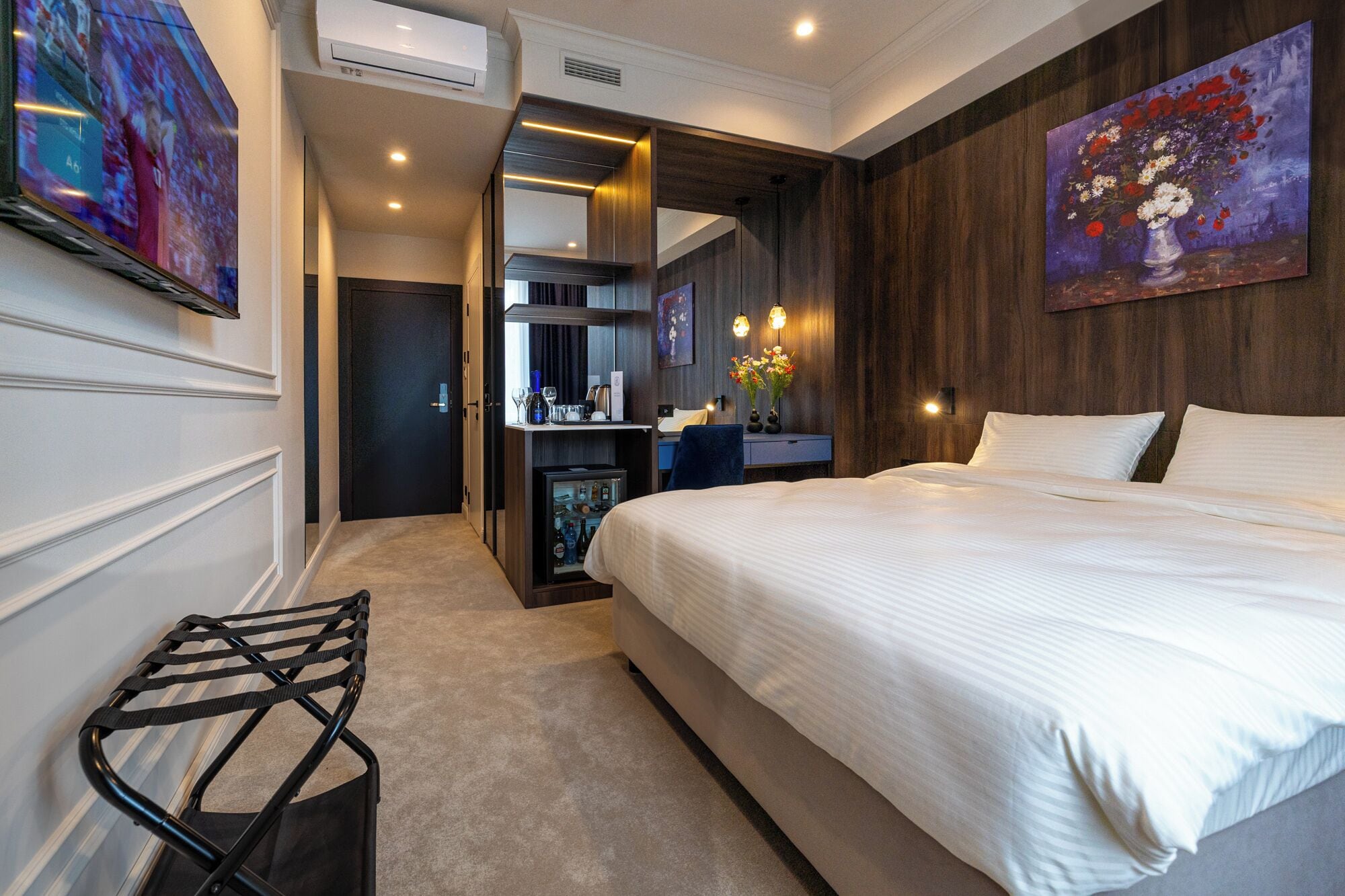 A modern hotel room with a large bed, a desk with a computer, and a seating area with a chair.