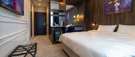 A modern hotel room with a large bed, a desk with a computer, and a seating area with a chair.