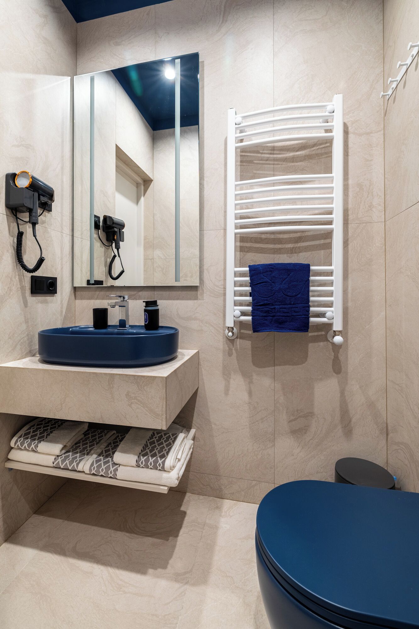 Un baño moderno con lavamanos empotrado, un perchero con una toalla azul y un espejo.