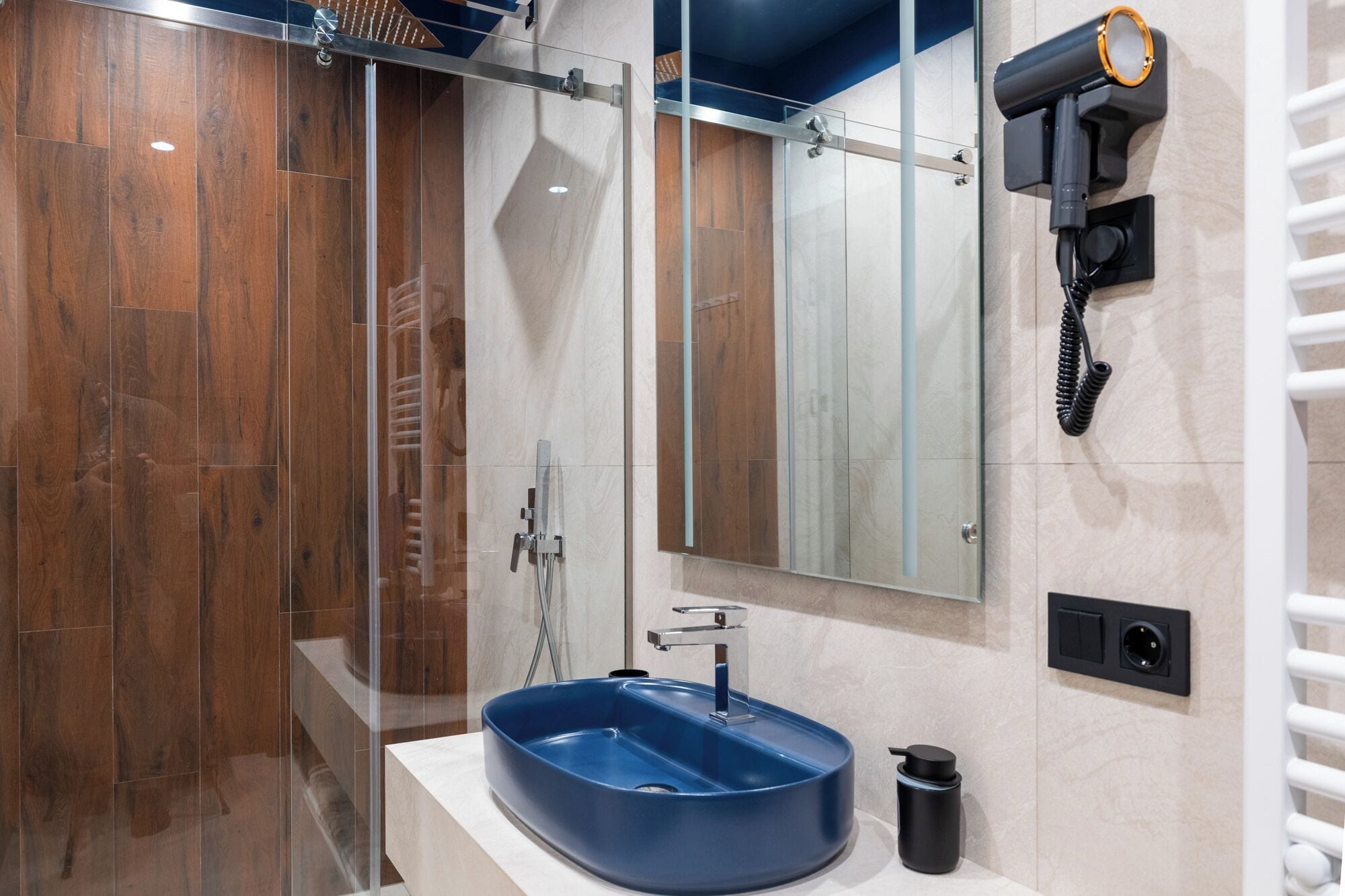 Un baño moderno con cabina de ducha de vidrio, un lavamanos azul y un secador de pelo montado en la pared.
