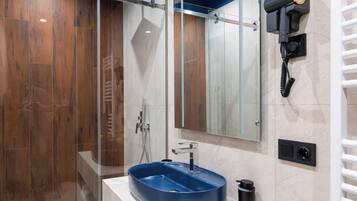 Un baño moderno con cabina de ducha de vidrio, un lavamanos azul y un secador de pelo montado en la pared.