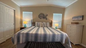 Une chambre à coucher comprenant un lit, deux lampes de chevet, une commode et une sculpture de poisson fixée au mur.