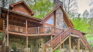 Una cabaña de troncos con base de piedra, balcones de madera y una escalera que lleva al nivel superior.