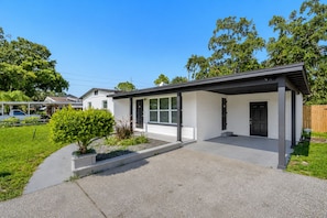 A modern single-story house with a covered porch, a small front yard with a bush, and a clear sky.