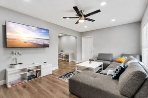 A modern living room with a flat-screen TV, a ceiling fan, a grey sofa, and a white coffee table.