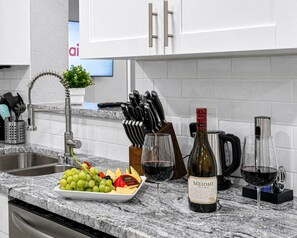 A kitchen counter with a wine bottle, glasses, a fruit platter, and kitchen utensils.