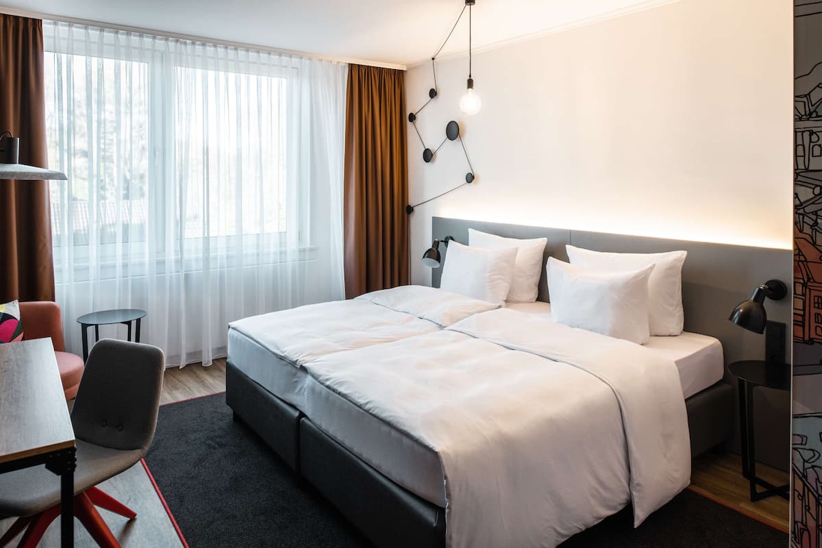 A modern hotel room with a large bed, a desk, and a chair.
