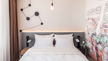 A modern hotel room with a neatly made bed, a wall-mounted light fixture, and a colorful cityscape mural.