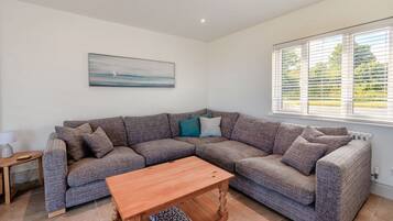 A modern living room with a sectional sofa, a wooden coffee table, a side table, and a window with blinds.