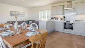Una cocina moderna con armarios blancos, una mesa de comedor para cuatro personas y vista al área de estar.