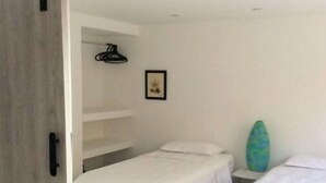 Ein Zimmer mit zwei Betten, einem Kleiderschrank, einem gerahmten Bild und einem Surfbrett.