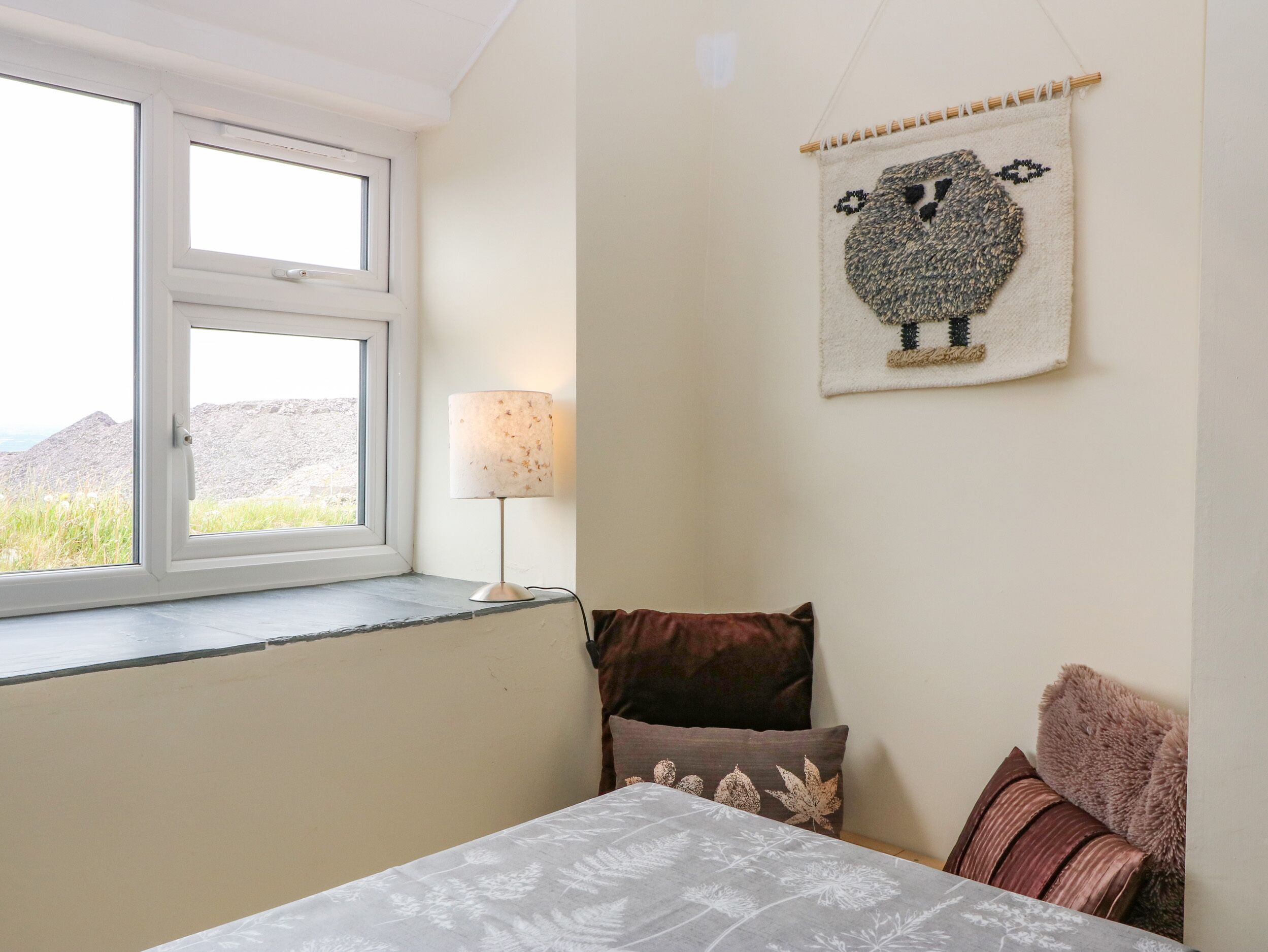 A bedroom with a bed, a window, a lamp, and a wall hanging.