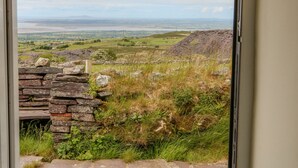 Un mur de pierre et une vue sur un paysage rural, avec des champs et une étendue d’eau visible au loin.