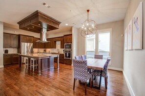 A modern kitchen with a central island, stainless steel appliances, and a dining area with patterned chairs. - Southern Charm Meets Easy Convenience, 5 mins to DT (Houston)
