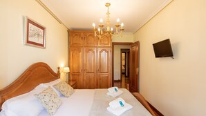 A hotel room with a wooden bed, a chandelier, a framed picture, and a television on the wall. - Plaza berri - baskeyrentals (Azkoitia)