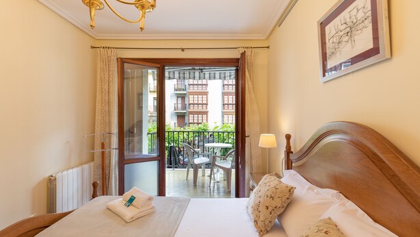 A hotel room with a bed, a chandelier, a view of the outside balcony, and a framed picture on the wall. - Plaza berri - baskeyrentals (Azkoitia)
