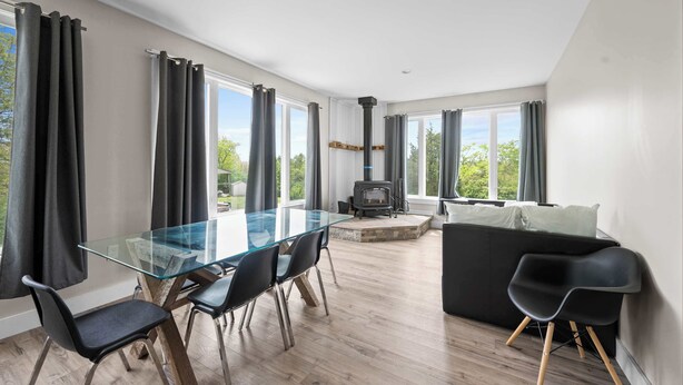Una sala de estar moderna con una mesa de comedor de vidrio, sillas negras, un sofá negro y una estufa de leña.