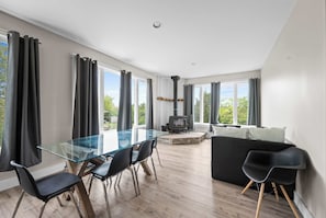 Una sala de estar moderna con una mesa de comedor de vidrio, sillas negras, un sofá negro y una estufa de leña.