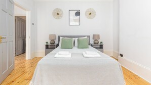 Een keurig opgemaakt slaapkamer met een groot bed, twee nachtkastjes en een kunstwerk in een lijst erboven.