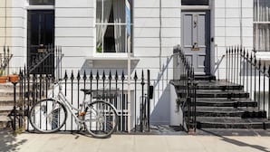 Een wit herenhuis met een zwarte fiets ervoor, een zwart ijzeren hek en een traprij die naar de ingang leidt.
