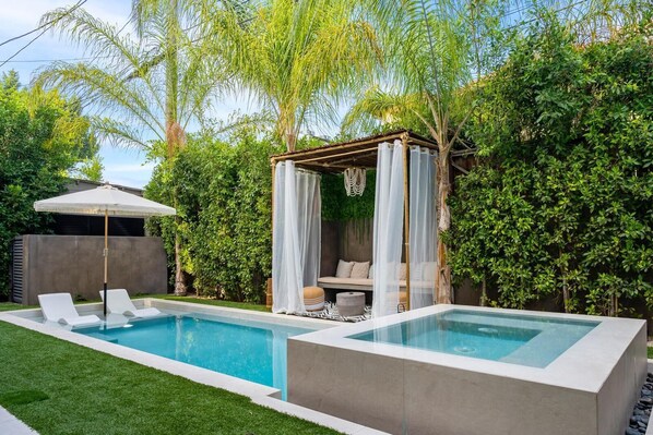 A modern outdoor pool area with a glass-enclosed hot tub, lounge chairs, and a canopy-covered seating area.
