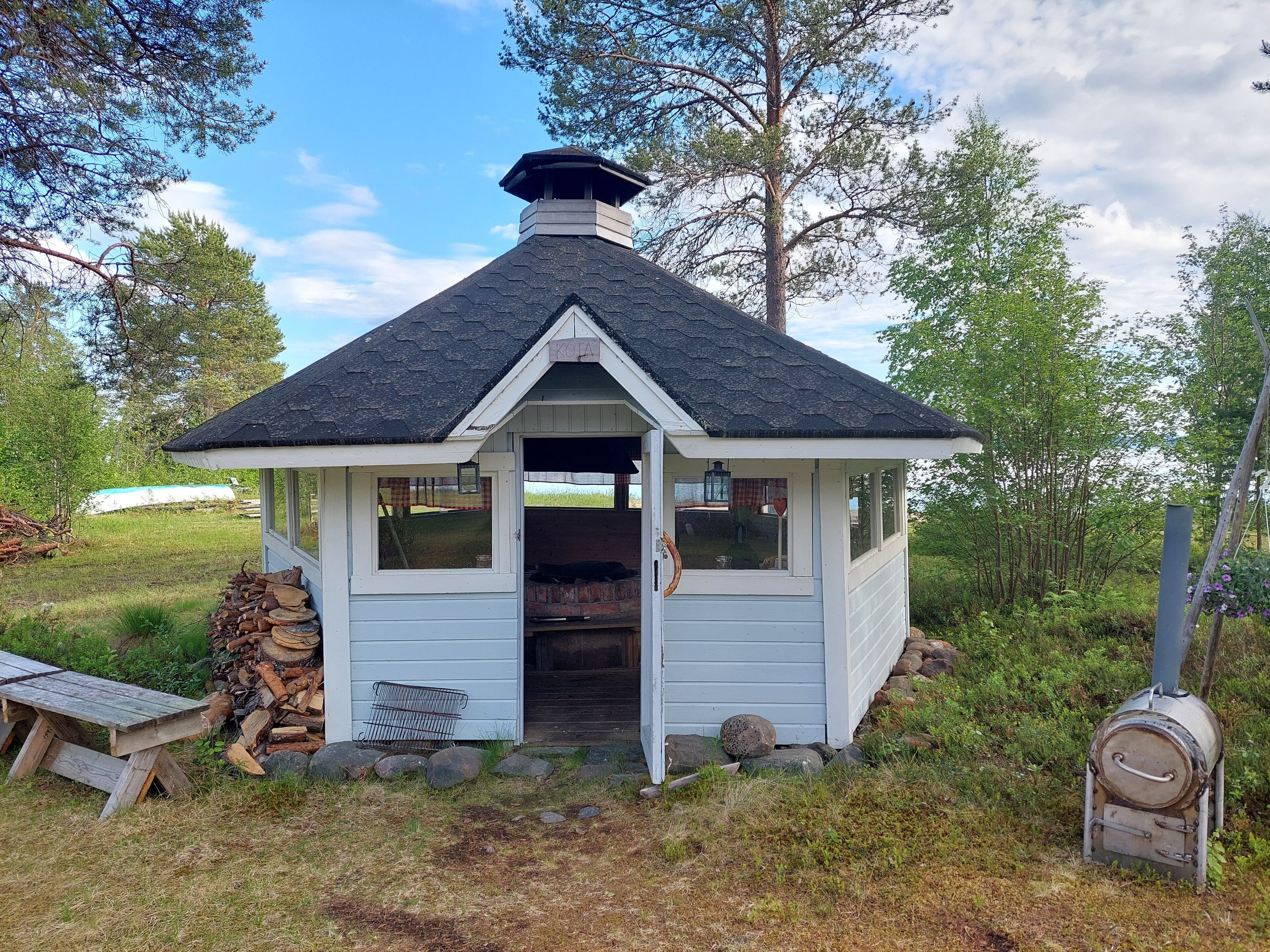 A small, white wooden structure with a dark roof, a chimney, and a door leading inside.