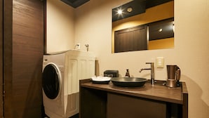 Een kleine wasruimte met een wasmachine, een wasbak, een koffiezetapparaat en een klein kastje.