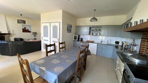 Un comedor con una mesa lista para cuatro, una cocina con electrodomésticos modernos y una sala de estar con sofá y televisor.