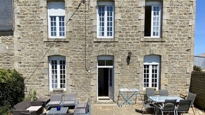 Edificio de piedra con puerta principal, ventanas y un patio con mobiliario exterior.