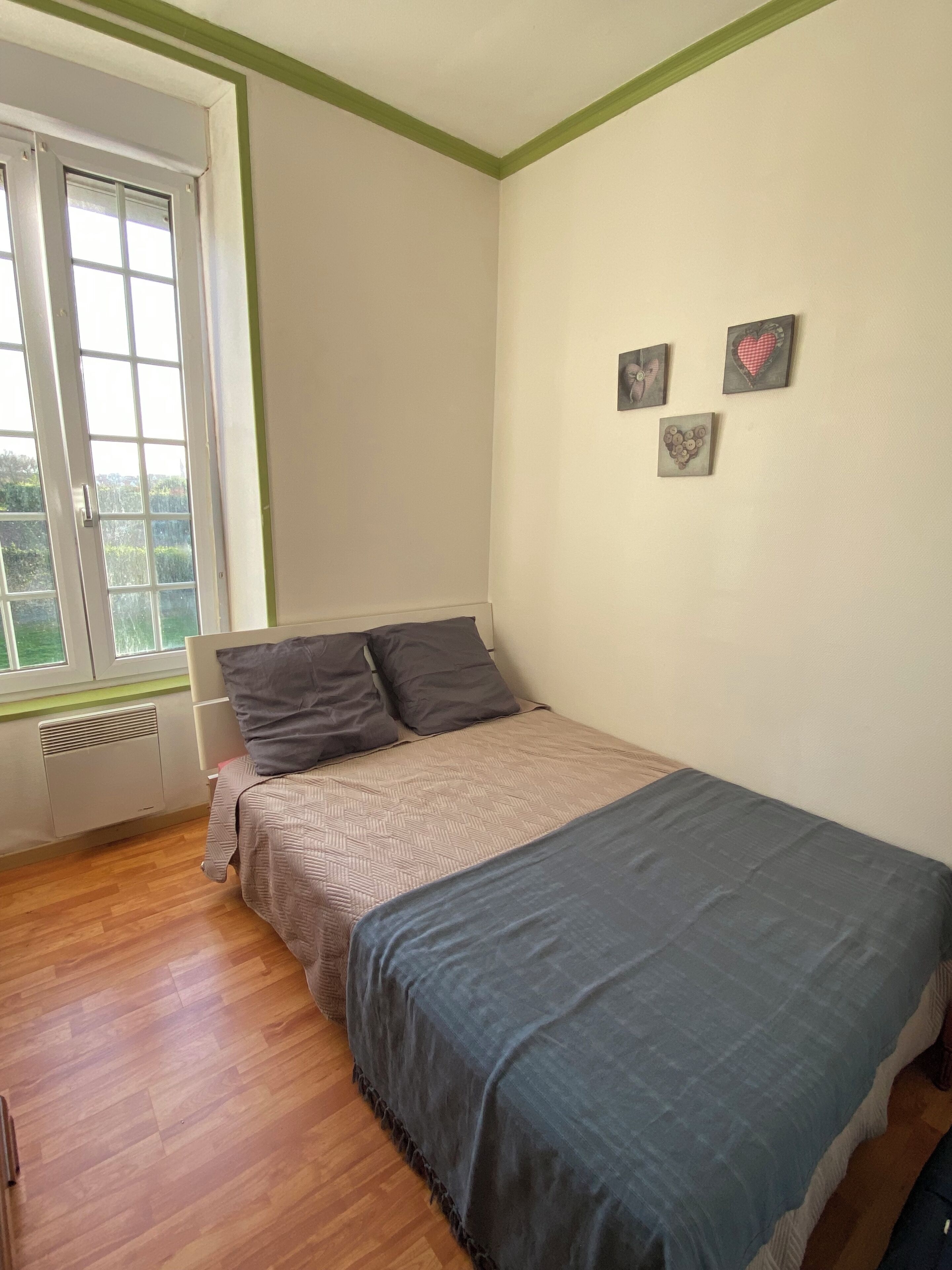 A bedroom with a bed, a radiator, a window, and a wall with three small pictures.