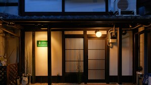 A traditional Japanese building with a wooden entrance, a signboard, and a small garden area with gravel and plants. - TSUBOMI luxury Inn shimabara-bettei 3 (Kyoto)
