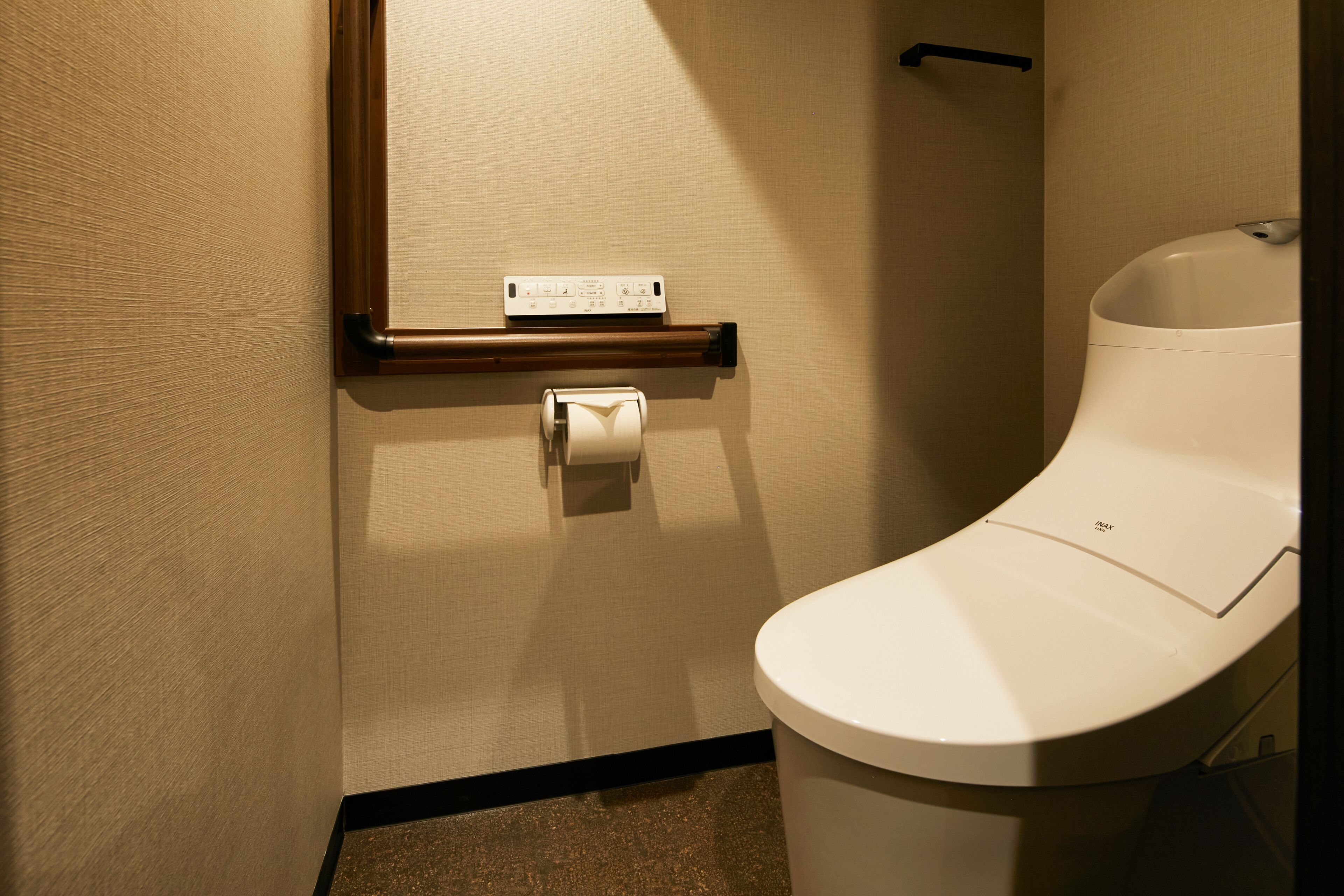 A modern bathroom with a toilet, a hand dryer, and a paper towel dispenser.