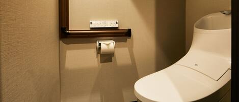 A modern bathroom with a toilet, a hand dryer, and a paper towel dispenser.