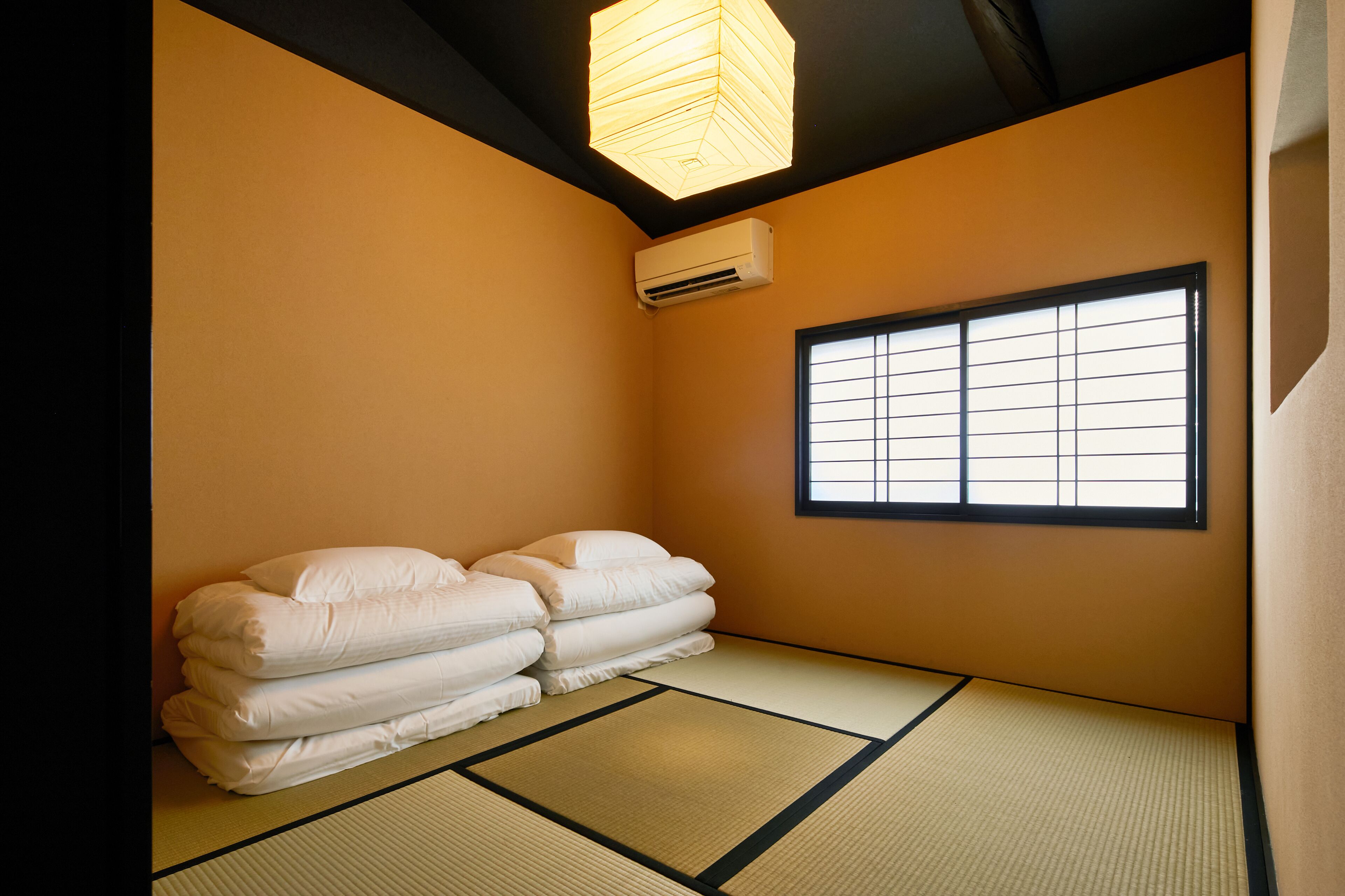 A traditional Japanese room with tatami flooring, a shoji screen window, and a stack of futons.