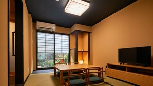 A traditional Japanese room with tatami flooring, a low table with cushions, a television on a wooden stand, and a sliding door leading to a garden. - TSUBOMI luxury Inn shimabara-bettei 3 (Kyoto)