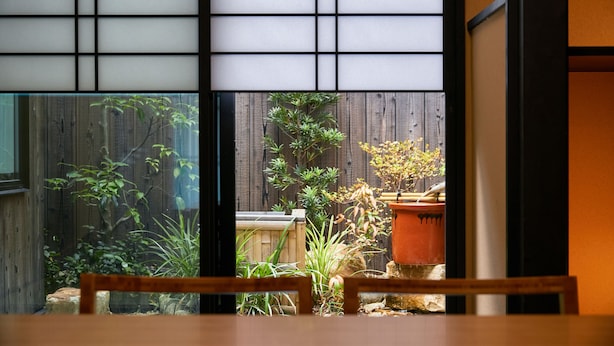 A view through a shoji screen into a garden with various plants and a wooden fence. - TSUBOMI luxury Inn shimabara-bettei 3 (Kyoto)