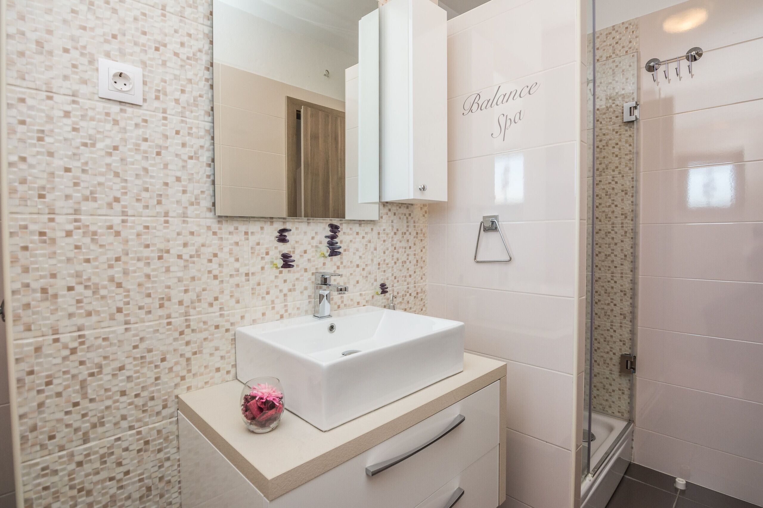A bathroom with a white sink, a mirror, and a shower area.