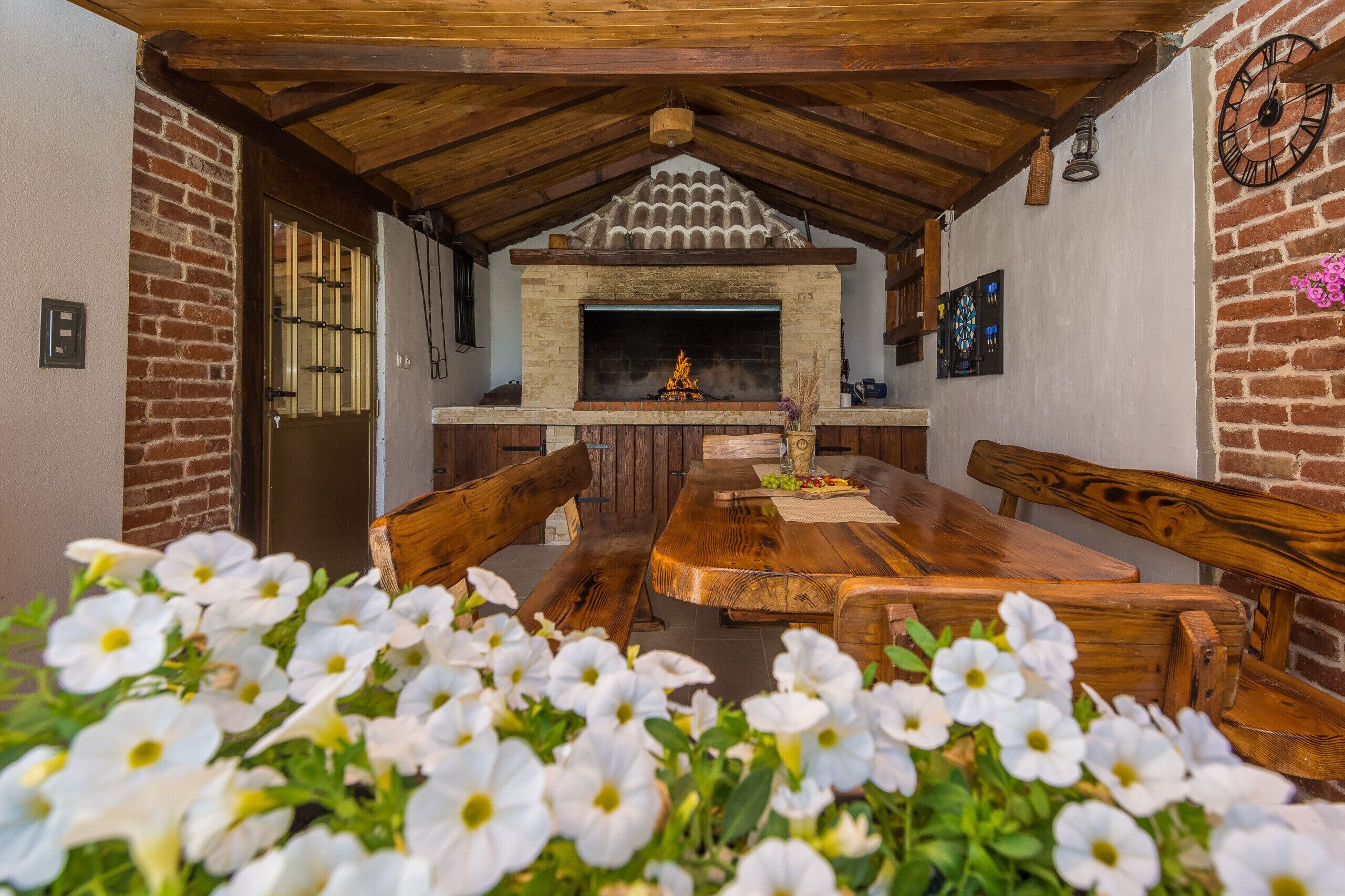 Un'area pranzo rustica con camino in mattoni, mobili in legno e fiori bianchi in primo piano.