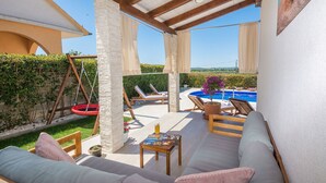 A covered outdoor seating area with a pool, lounge chairs, and a swing set. - Villa M&M (Pakostane)