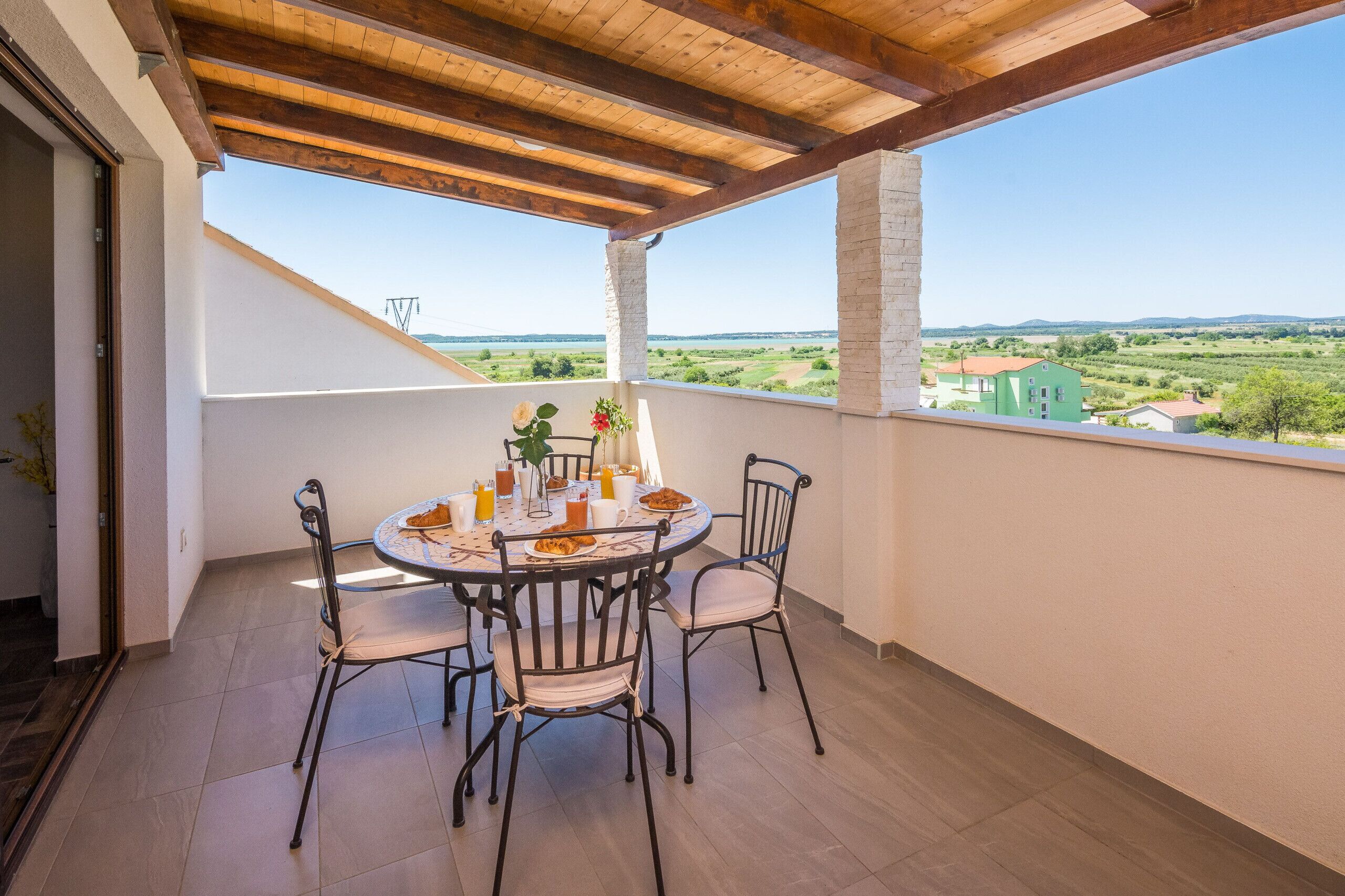 A balcony with a round table, chairs, and a view of the countryside.