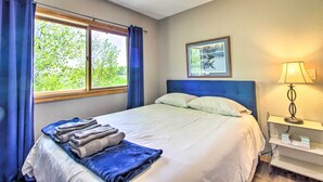 Una habitación de hotel con cama, ventana con cortinas, lámpara de noche y un cuadro en la pared.