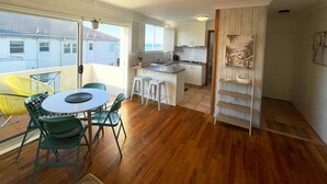 Une cuisine moderne avec des meubles blancs, un coin repas doté d’une table ronde et de chaises vertes, et une vue sur la mer grâce à de grandes fenêtres.