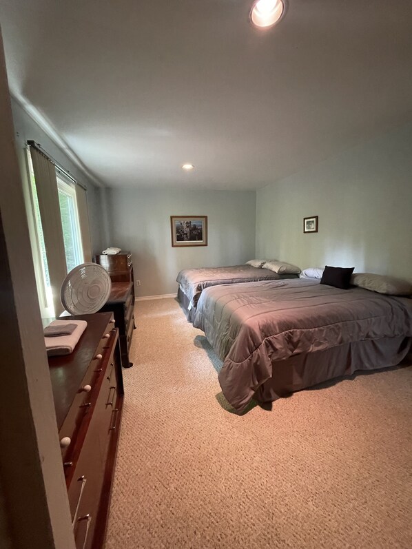 A bedroom with two beds, a dresser, a fan, and a window with curtains. - Cabin in the woods (Wolverine)