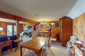Un accogliente interno di una baita con un tavolo da pranzo in legno, sedie, angolo cottura e un'area giochi per bambini.