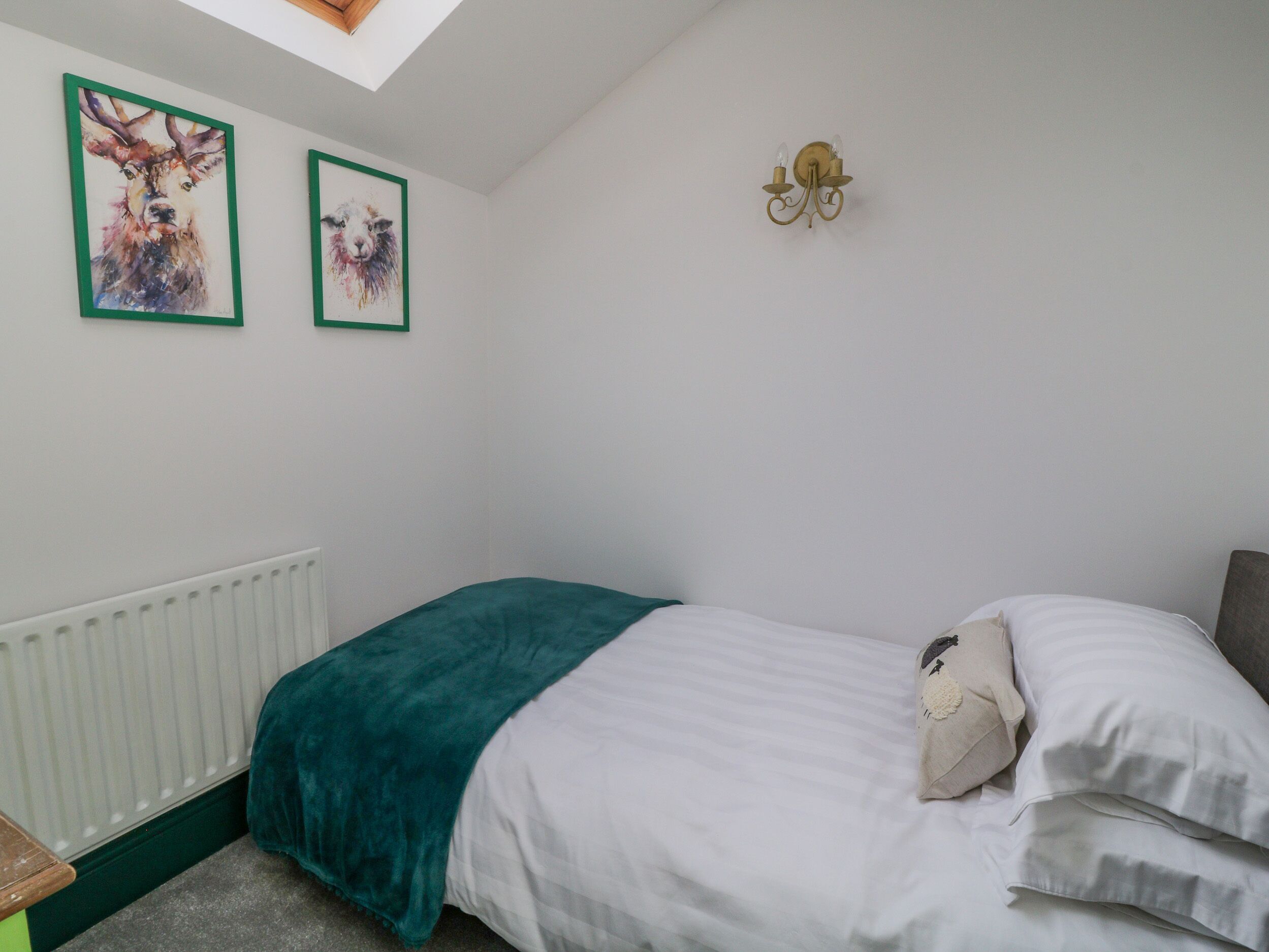Une chambre à coucher comprenant un lit, un radiateur, deux tableaux représentant des animaux encadrés et un luminaire fixé au mur.