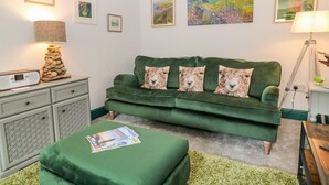 A cozy living room with a green sofa, a lamp, and framed artwork on the walls. - Herdwick Cottage (Brampton)