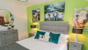 A bedroom with a grey tufted headboard, a white bedspread, and green pillows. There are two bedside tables with lamps and a dresser with a mirror. - Herdwick Cottage (Brampton)